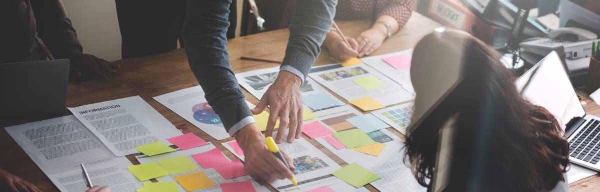 Men and women surround a table covered in various business-related sheets that include Venn diagrams, reports, and images.