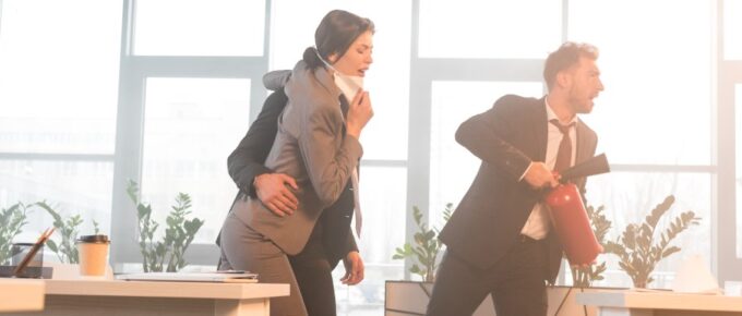 Three workers run in an office building during an emergency. The one leading the group holds a fire extinguisher.