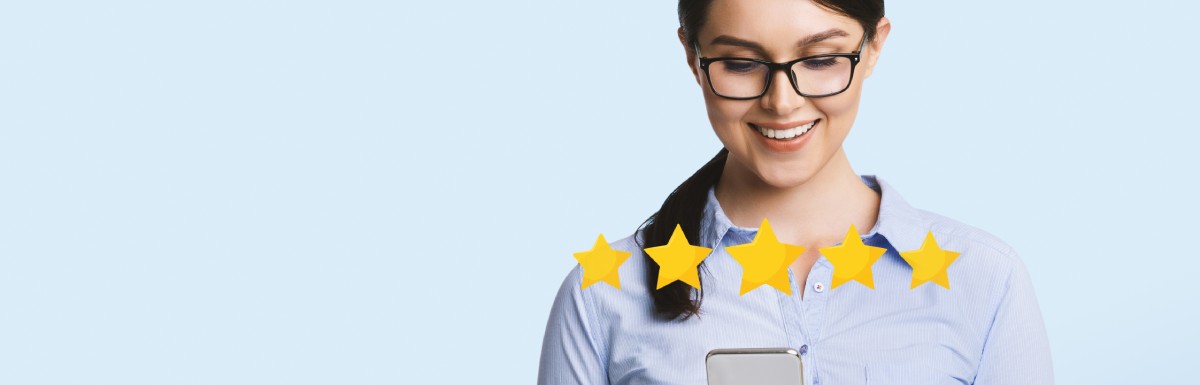 A woman wearing glasses and a blue shirt is standing and smiling at her phone. There are five stars above the phone.