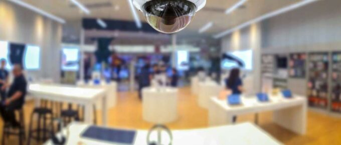 A CCTV security camera on the ceiling of an audio equipment retail shop. Employees and customers are seen in the background.