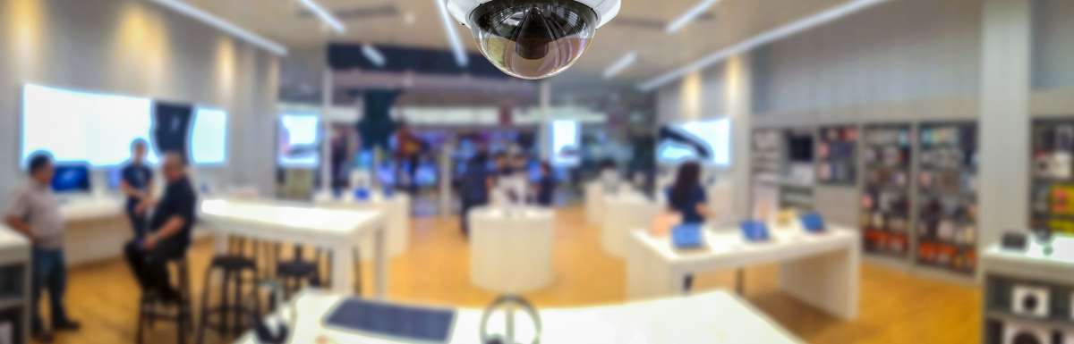 A CCTV security camera on the ceiling of an audio equipment retail shop. Employees and customers are seen in the background.