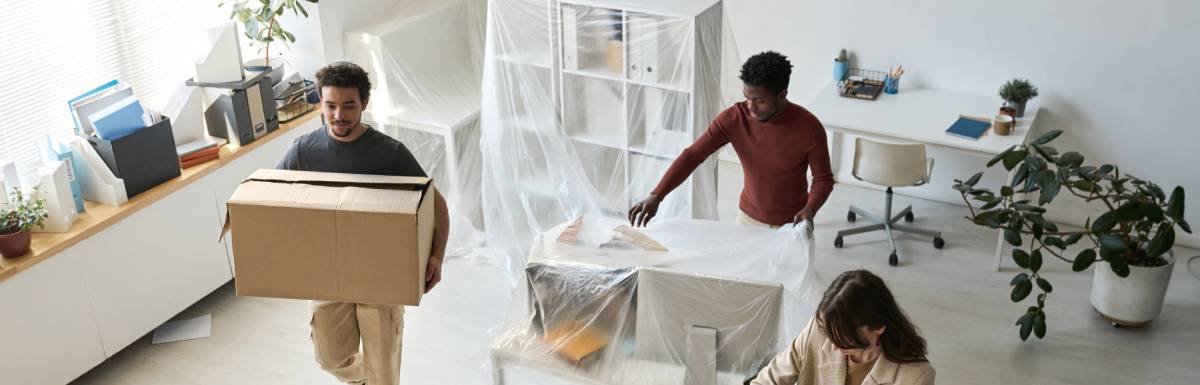 A high-angle view of two men and one woman packing and moving equipment from a brightly lit office space.