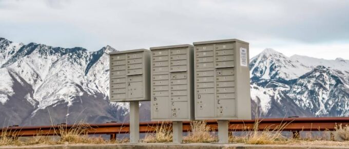 A multi-tenant freestanding mailbox stands alongside a road with a gorgeous snow-covered mountain behind it.