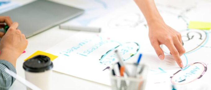 A hand points to a word on a word map laying on a table with several people gathered around it.