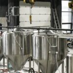 Modern brewery interior with stainless steel fermentation tanks, automated equipment, and industrial design elements.