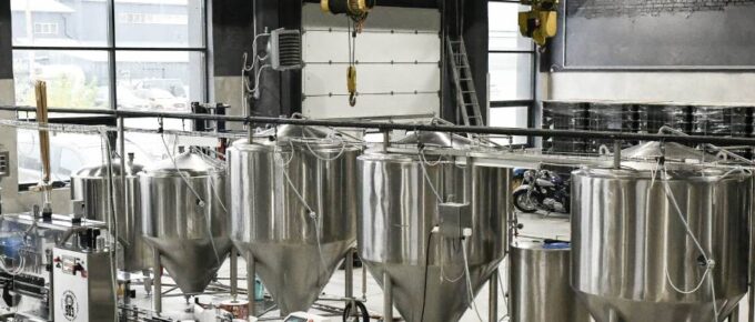 Modern brewery interior with stainless steel fermentation tanks, automated equipment, and industrial design elements.