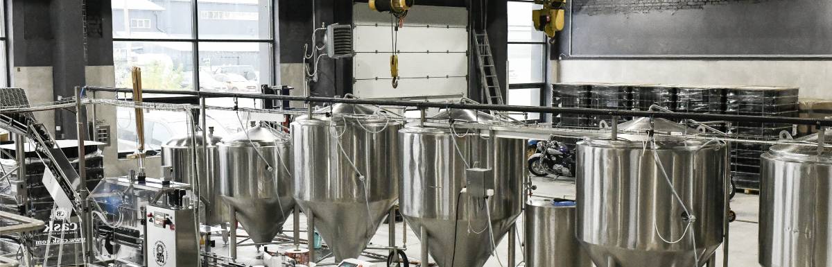 Modern brewery interior with stainless steel fermentation tanks, automated equipment, and industrial design elements.