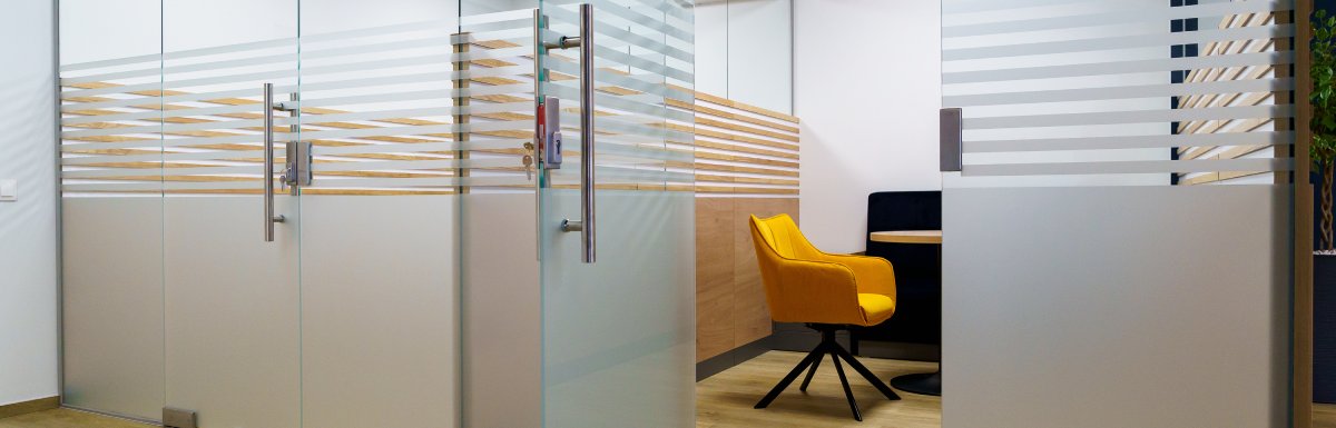 A space in an office separated by glass doors. The space has a yellow cushioned chair and a table.