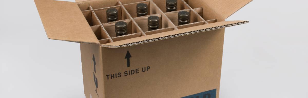 A cardboard box with bottles inside slots. The box is labeled with "This side up, Glass fragile handle with care, and cold room."