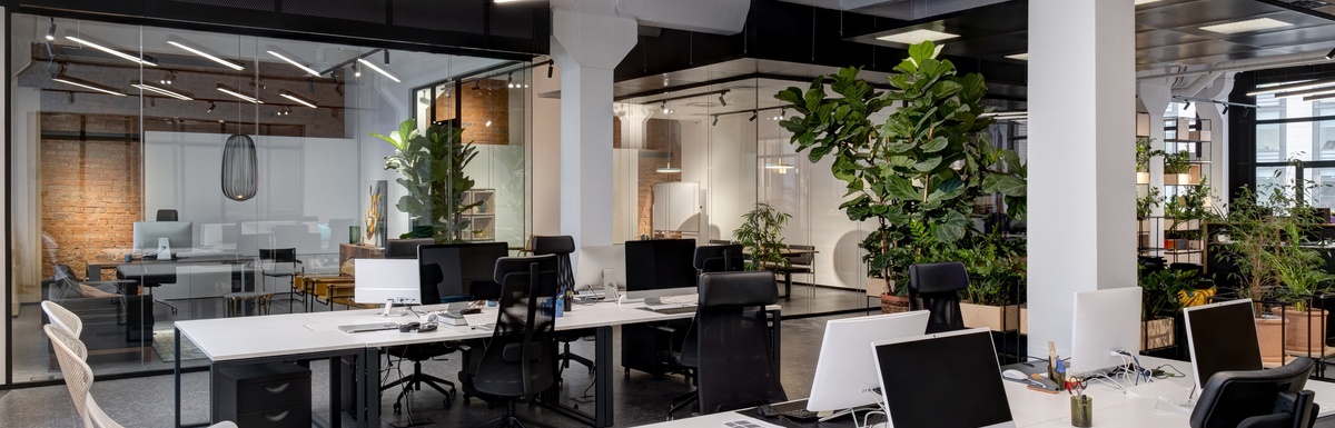 An open concept office has two large workstations with several monitors and keyboards. The devices' wires neatly go into grommets.