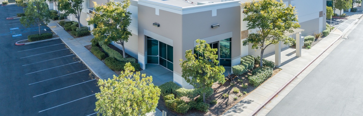 The sun shines on a large, one-story industrial office building with landscaped beds and an empty parking lot.