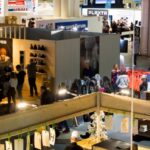 An aerial view of a large trade show. Attendees walk between different booth areas.