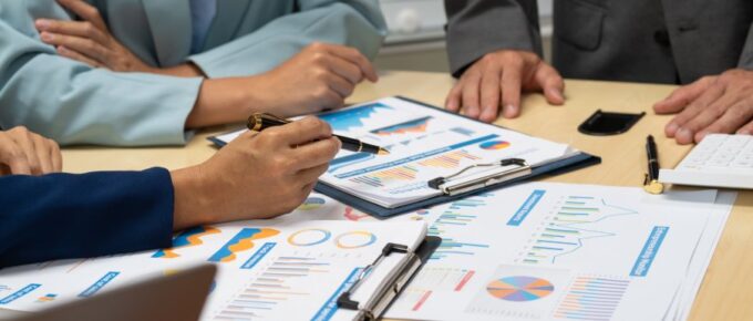 Three people dressed in business attire at a table looking over papers full of charts, graphs, and other information.