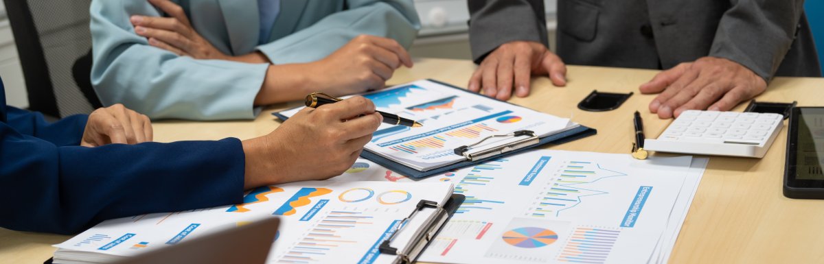 Three people dressed in business attire at a table looking over papers full of charts, graphs, and other information.