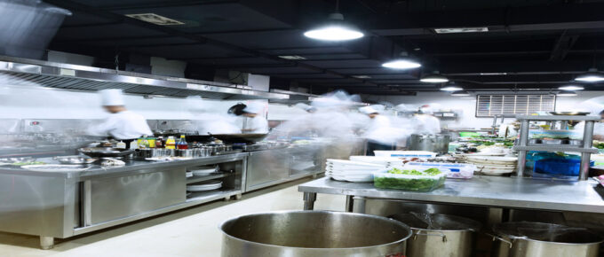 A busy commercial kitchen with multiple chefs dressed in white moving from station to station.