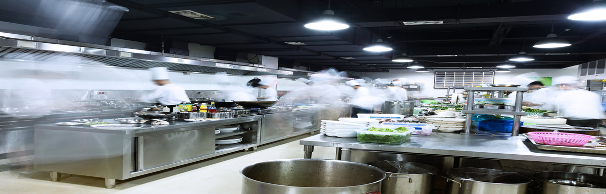 A busy commercial kitchen with multiple chefs dressed in white moving from station to station.