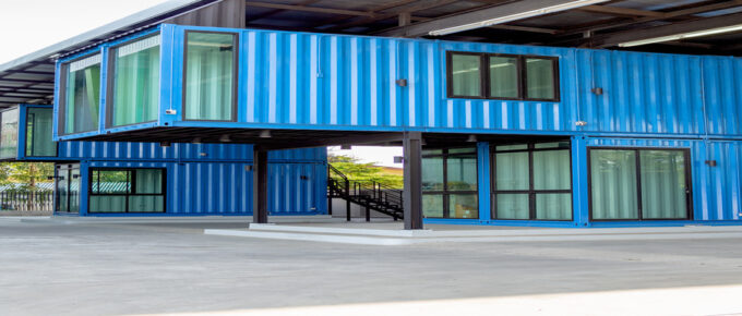 Two two-story blue shipping container offices sit next to each other. There are plenty of windows with closed curtains.