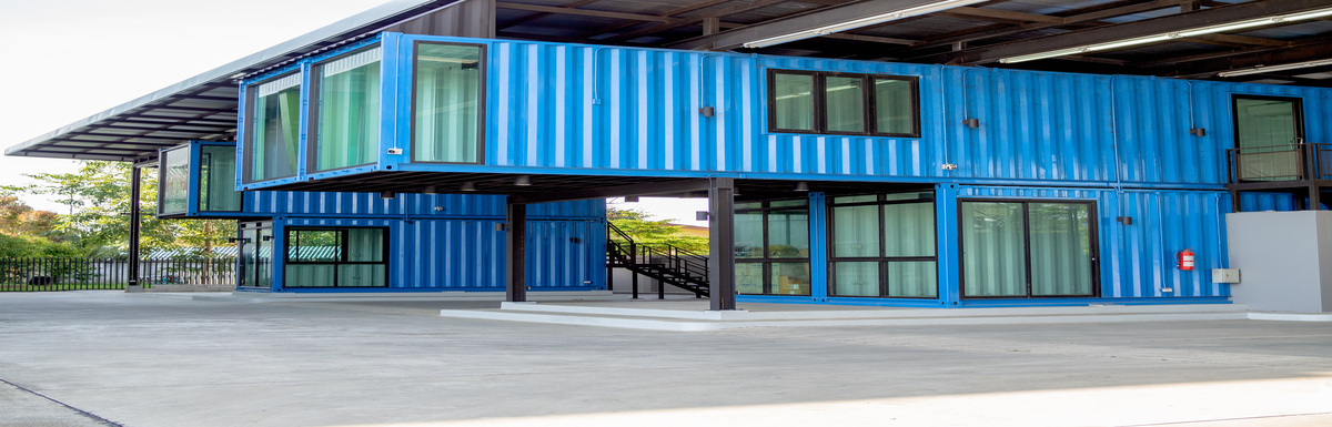 Two two-story blue shipping container offices sit next to each other. There are plenty of windows with closed curtains.
