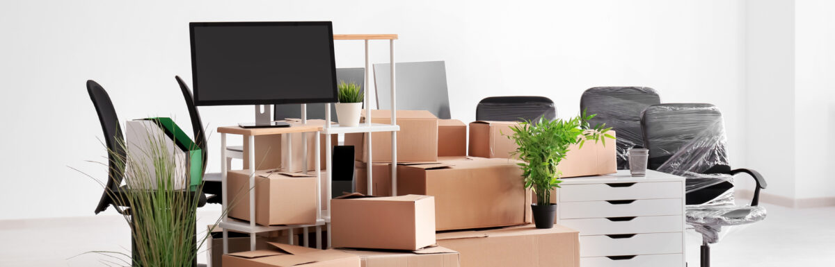 A pile of boxes and office supplies, including shelving units and rolling desk chairs wrapped in plastic.