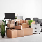 A pile of boxes and office supplies, including shelving units and rolling desk chairs wrapped in plastic.