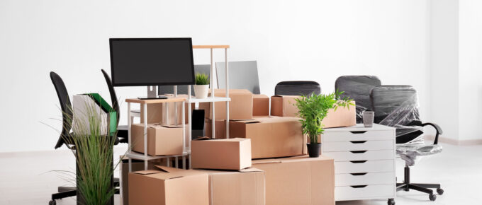 A pile of boxes and office supplies, including shelving units and rolling desk chairs wrapped in plastic.