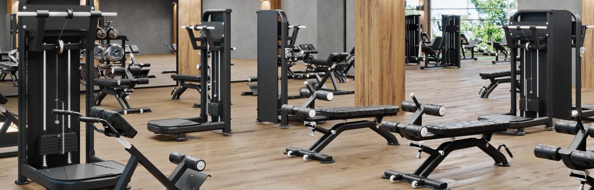 The inside of a modern gym with a black ceiling, wooden beams, and several exercise machines and benches on the floor.