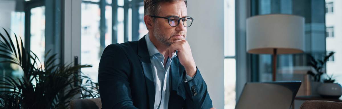 A businessman uses a laptop for online reading, with a facial expression that indicates he's engaged in problem-solving.