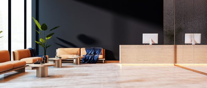 A spacious reception area with a bright-tan theme and warm lighting. Orange sofas and floor plants line the sides.