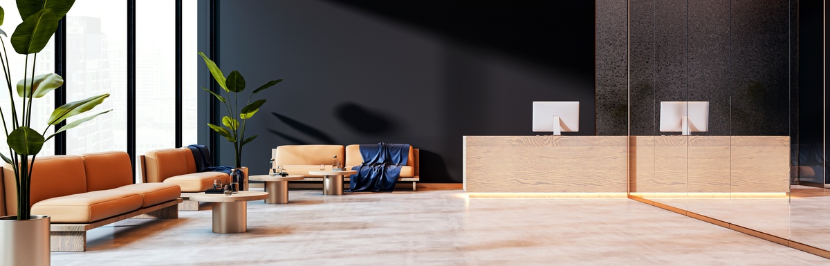 A spacious reception area with a bright-tan theme and warm lighting. Orange sofas and floor plants line the sides.
