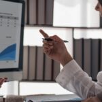 Businesspeople discuss project planning with a colleague about a financial report on the woman's laptop.