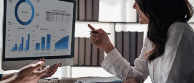 Businesspeople discuss project planning with a colleague about a financial report on the woman's laptop.