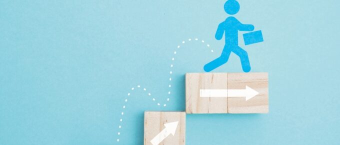 A conceptual depiction of upward career trajectory. A stick figure climbs a staircase of blocks leading upward.