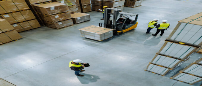 An overhead view of a warehouse storage space. There are multiple workers on the floor and a forklift.