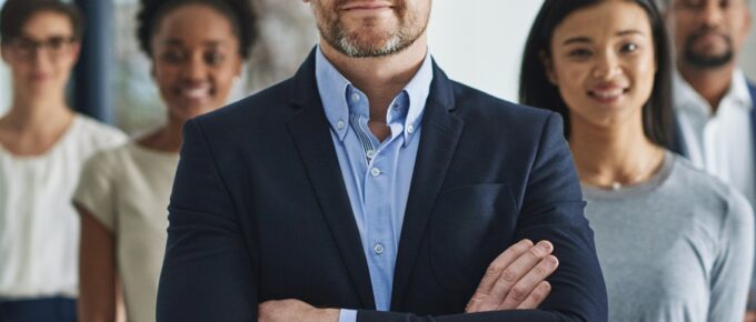A man in a blue suit and button-down shirt stands with his arms crossed in front of four smiling individuals.