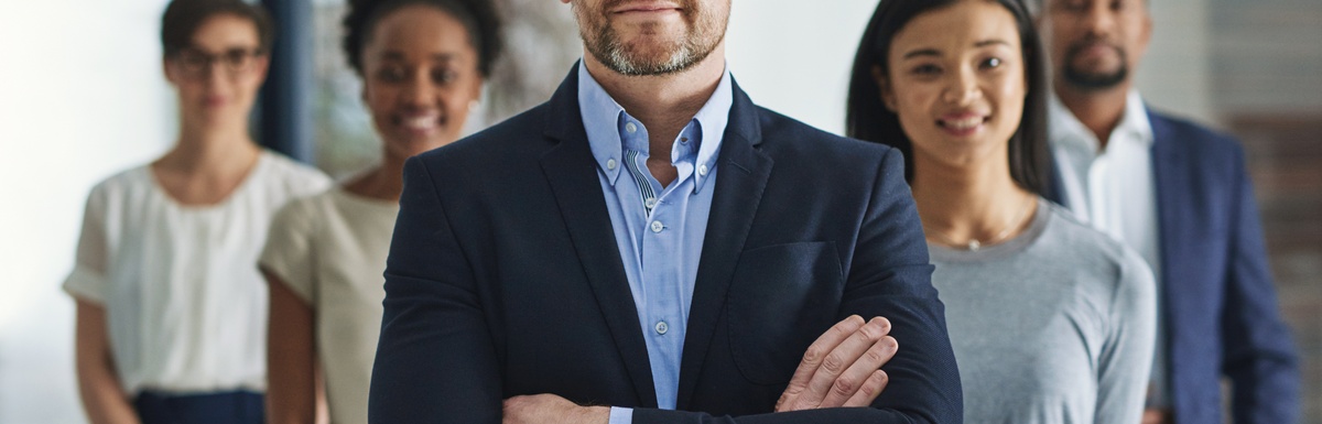 A man in a blue suit and button-down shirt stands with his arms crossed in front of four smiling individuals.