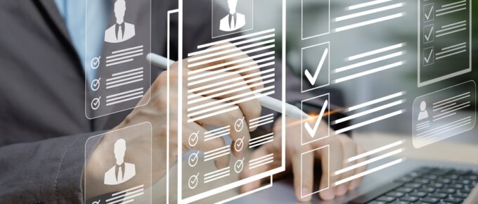 A person looking at a laptop with a notebook next to it. There is an overlay of resume icons for hiring someone.