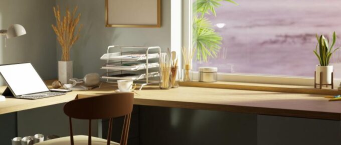 An L-shape desk sits in the corner of the room next to a window. There's a laptop on the shorter tabletop.
