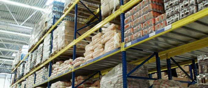 A ground view of a warehouse with industrial shelving. Products on pallets are stacked on the shelves.