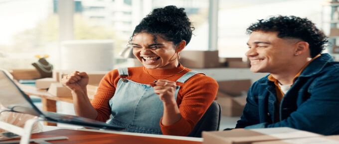 Two business partners are smiling and celebrating in front of the laptop while working in their living room.