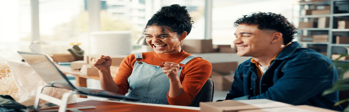 Two business partners are smiling and celebrating in front of the laptop while working in their living room.