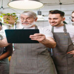 A group of employees gathering around a business professional holding a black tablet and giving instructions to them.