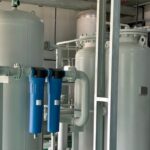 An industrial facility has multiple air compressor systems and filtration tanks. The floor is green.