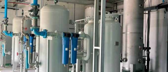 An industrial facility has multiple air compressor systems and filtration tanks. The floor is green.