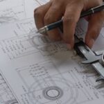 Someone measuring the size of a metal bearing. They are working on top of a stack of various blueprints.