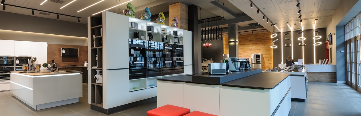 A modern retail showroom interior with sleek white display islands, contemporary lighting fixtures, wide walkways, and organized product displays in a spacious, open layout.