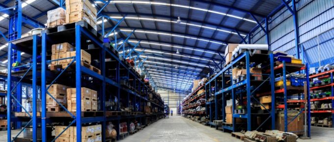 An expansive business warehouse with a number of blue shelves, all filled with crates and boxes, and wide aisles.