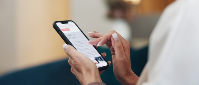 Someone holds a phone in front of them while they scroll through an ad. One of their fingers hovers over the screen.