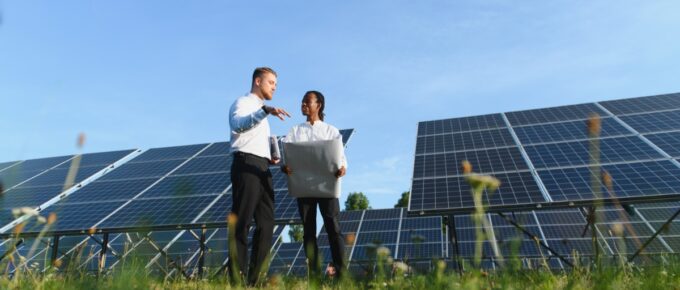 Two engineers standing beside solar panels while reviewing papers under a clear blue sky in a grassy field.