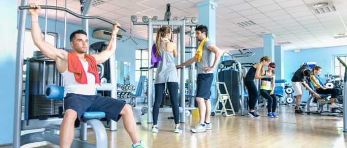 Several people exercising on strength training machines and working with trainers inside a bright, spacious gym.