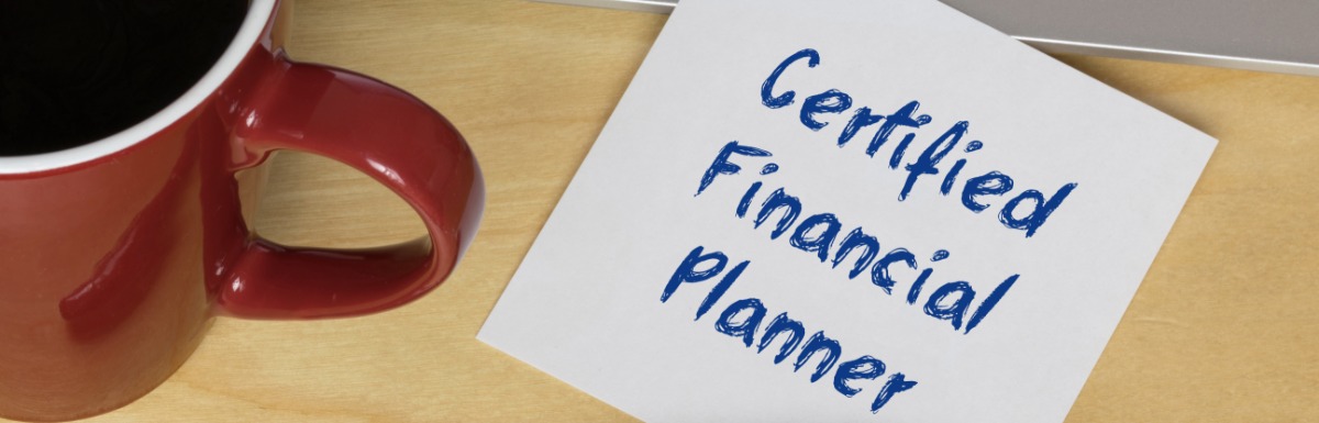 A close-up of a white sticky note with "Certified Financial Planner" written on it next to a pen and coffee mug.